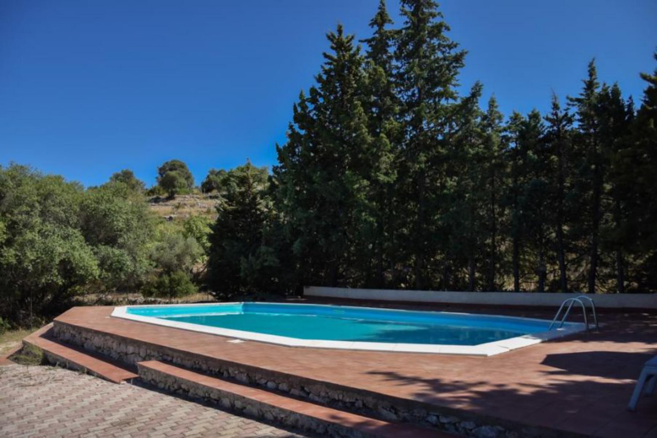 Une piscine rectangulaire bordée de pierres, entourée d’une terrasse en briques.