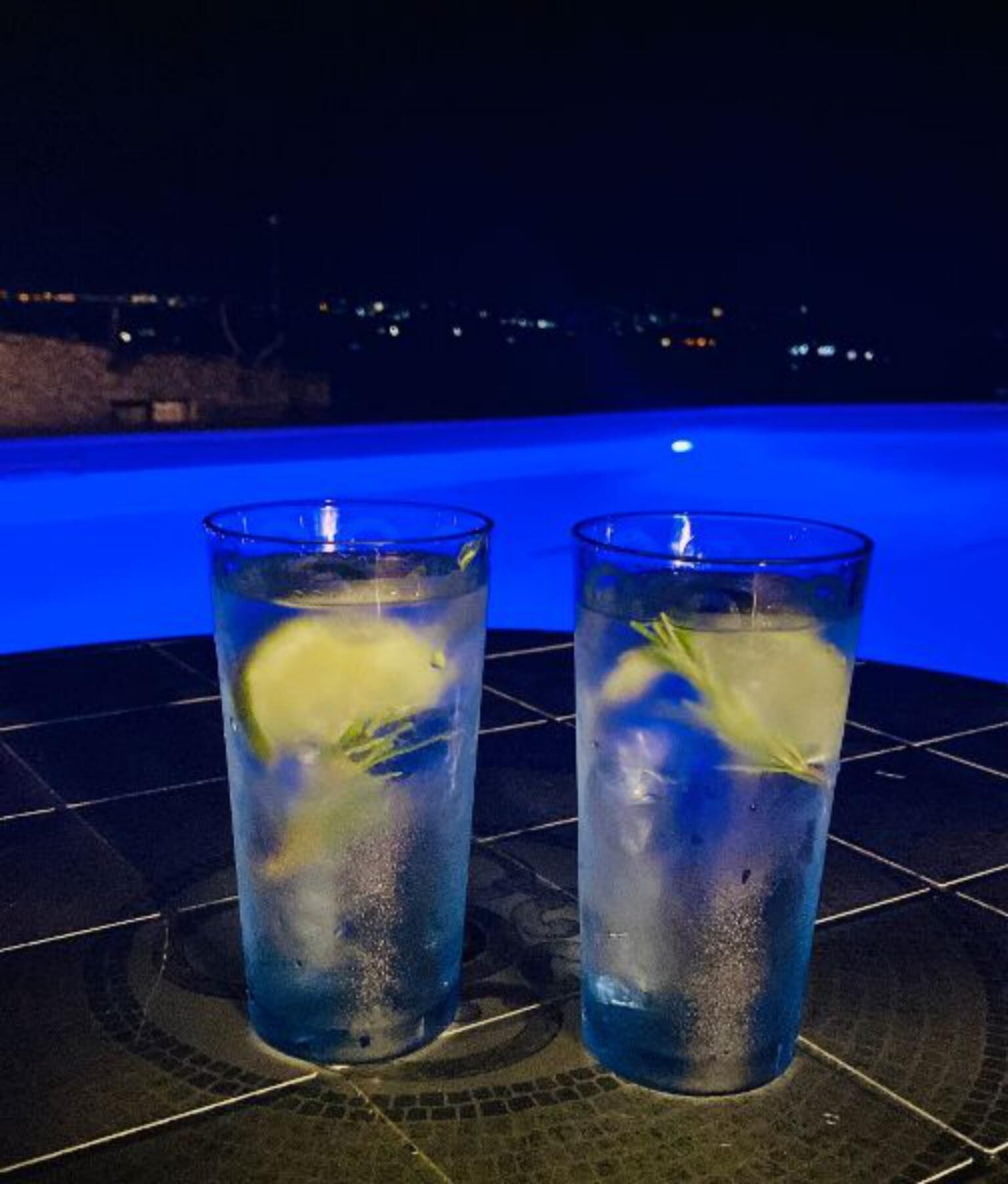 Two glasses of blue beverage with lemon slices on a tiled surface near a pool.