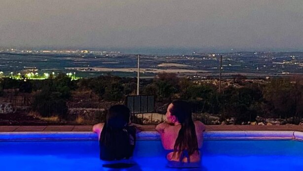 Two people sitting by a pool with a view of a distant cityscape. - Casale Cugni with swimming pool for exclusive use - air conditioned - wi-fi (Noto)
