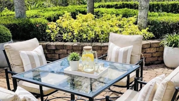 Une terrasse extérieure avec une table à plateau de verre, entourée de quatre chaises dotées de coussins.