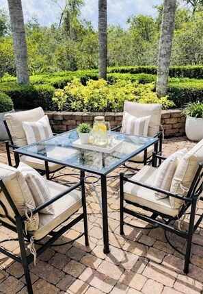 An outdoor patio with a glass-top table surrounded by four chairs with cushions.