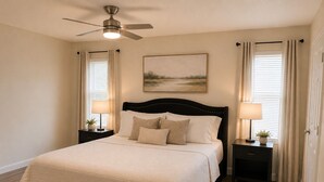 Une chambre à coucher avec un lit, des tables de chevet, un ventilateur de plafond et un tableau accroché au mur.