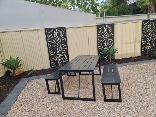 A patio area with a wooden table and benches, surrounded by a decorative fence and small plants. - Goolwa serenity, Great balcony, Modern, peaceful, water and attractions close by (Goolwa South)