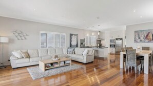 A modern living room with a sofa, coffee table, and a dining area with chairs. - Goolwa serenity, Great balcony, Modern, peaceful, water and attractions close by (Goolwa South)