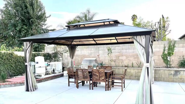 Une terrasse extérieure dotée d’un espace repas couvert, d’un barbecue et d’un mur en pierre en arrière-plan.