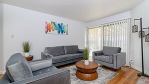 Un salon moderne avec un canapé gris, une table basse ronde en bois et un tableau abstrait aux couleurs vives accroché au mur.