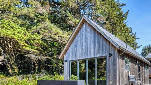 Een moderne houten chalet met een grote schuifglazen deur, een terras en een ingebouwde bank.