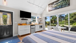 Une chambre d’hôtel moderne dotée d’un grand lit, d’une kitchenette, d’une télévision à écran plat et d’un balcon avec coin salon extérieur.