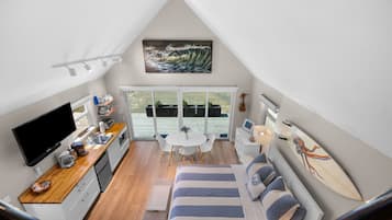 A compact room with a bed, a dining table, a TV, and a surfboard.