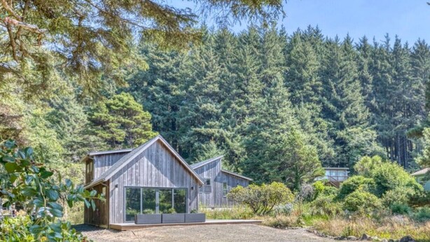 Une cabane en bois dotée d’une grande fenêtre en verre, entourée d’une forêt dense.
