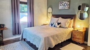 A bedroom with a large bed, two bedside tables, a chandelier, a painting, and a mirror.