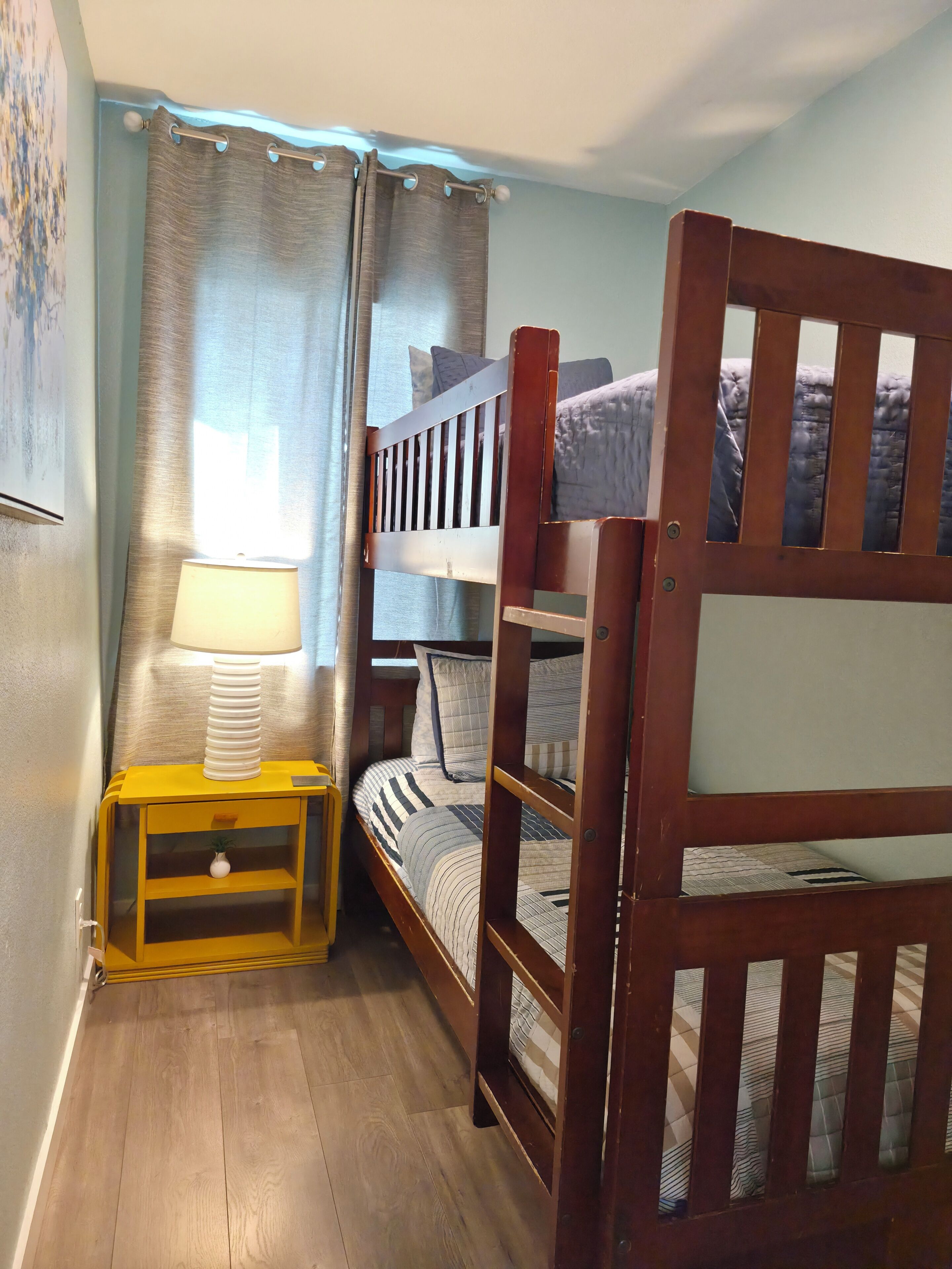 A bunk bed with a wooden frame, a bedside table with a lamp, and a wall-mounted shelf.