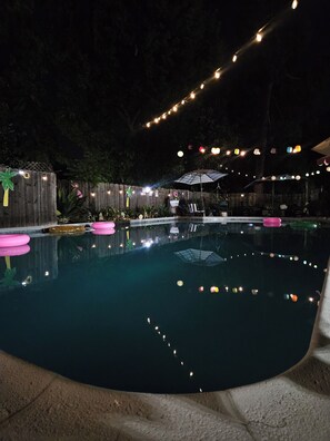 A swimming pool with a wooden deck, surrounded by a wooden fence and string lights. - Garden Clara (Yuba City)
