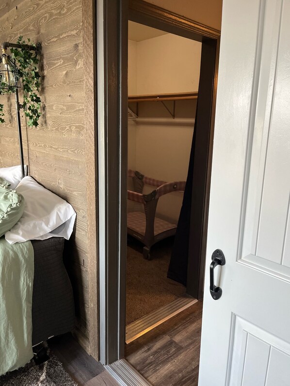 Un dormitorio con cama, mesita de noche, planta colgante y puerta que da a otra habitación.