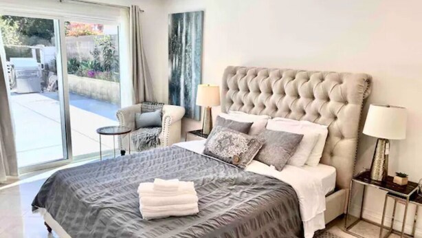 Une chambre avec un grand lit, deux tables de chevet, une chaise et une vue sur l’extérieur.