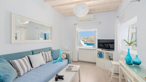 Un soggiorno moderno con un divano, un tavolino da caffè con una fotocamera, una TV e una finestra vista mare.