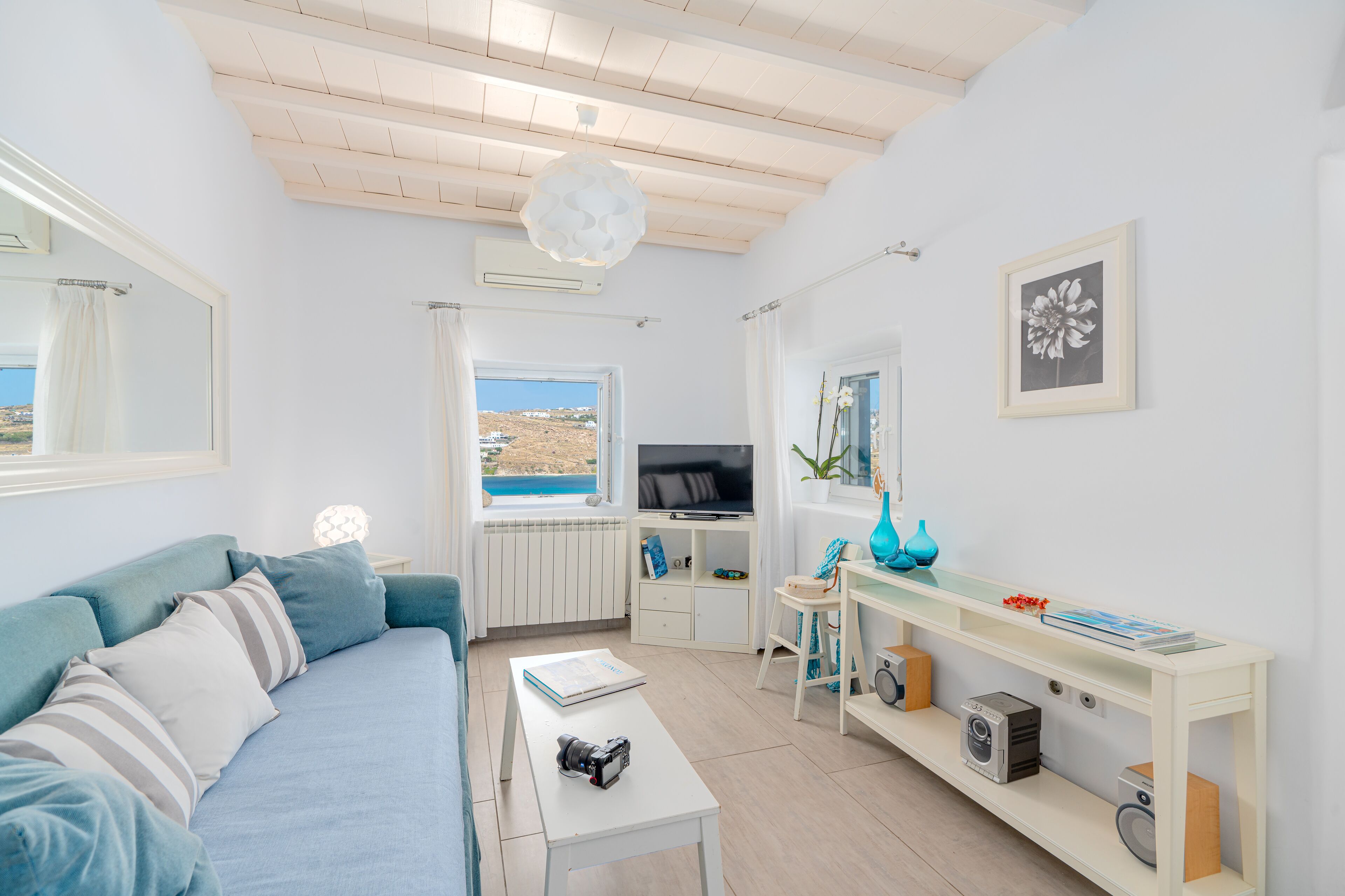 A modern living room with a sofa, a coffee table, a TV, and a view of the sea.