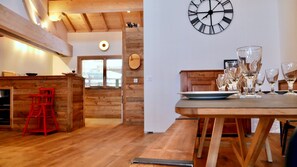 Um interior de madeira com uma mesa de jantar posta para refeição, um relógio de parede e uma cadeira vermelha.