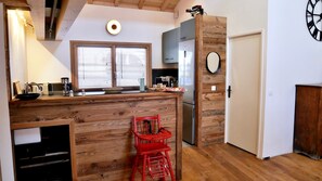 Una cucina con mobili in legno, un'isola integrata con sgabelli, un frigorifero e un'ampia finestra con persiane.