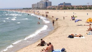 A beach with people sunbathing and swimming, a few umbrellas, and buildings in the background.