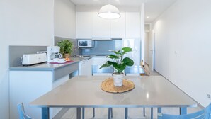 A modern kitchen with white cabinets, a microwave, a toaster, and a coffee maker. There is a dining table with a woven placemat and a potted plant.