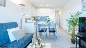 A modern living room with a blue sofa, a dining table with chairs, a kitchen area, and a large potted plant.