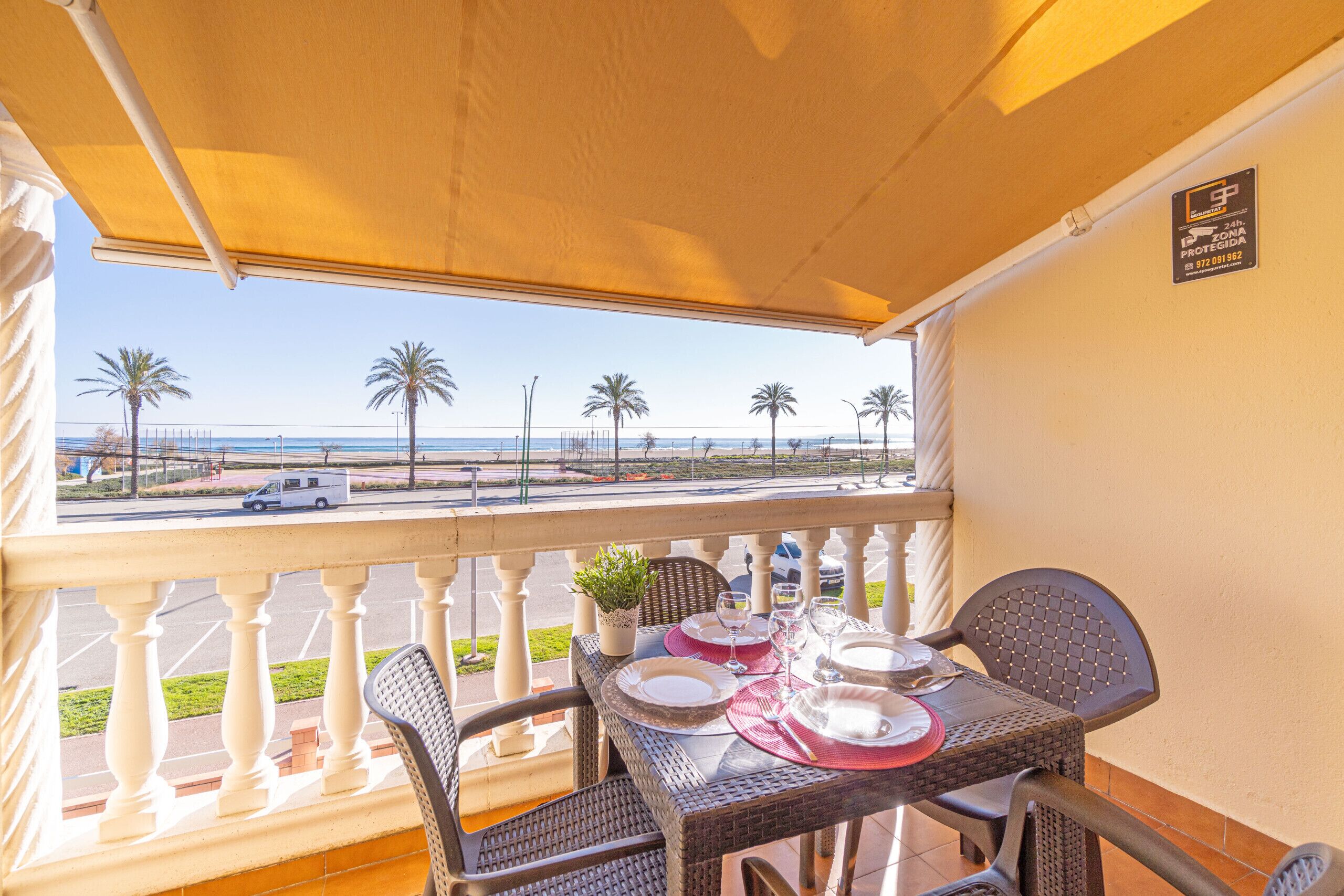 Un balcone con un tavolo apparecchiato per mangiare, con vista su una spiaggia, palme e una strada.