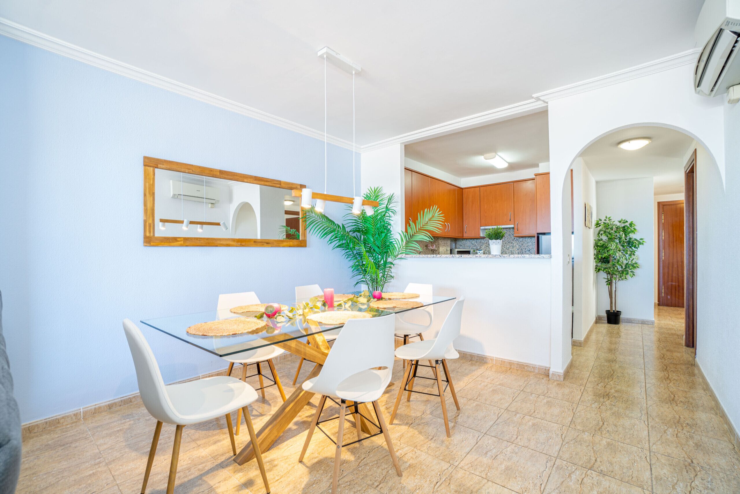 A dining area with a glass table, white chairs, and a potted plant.