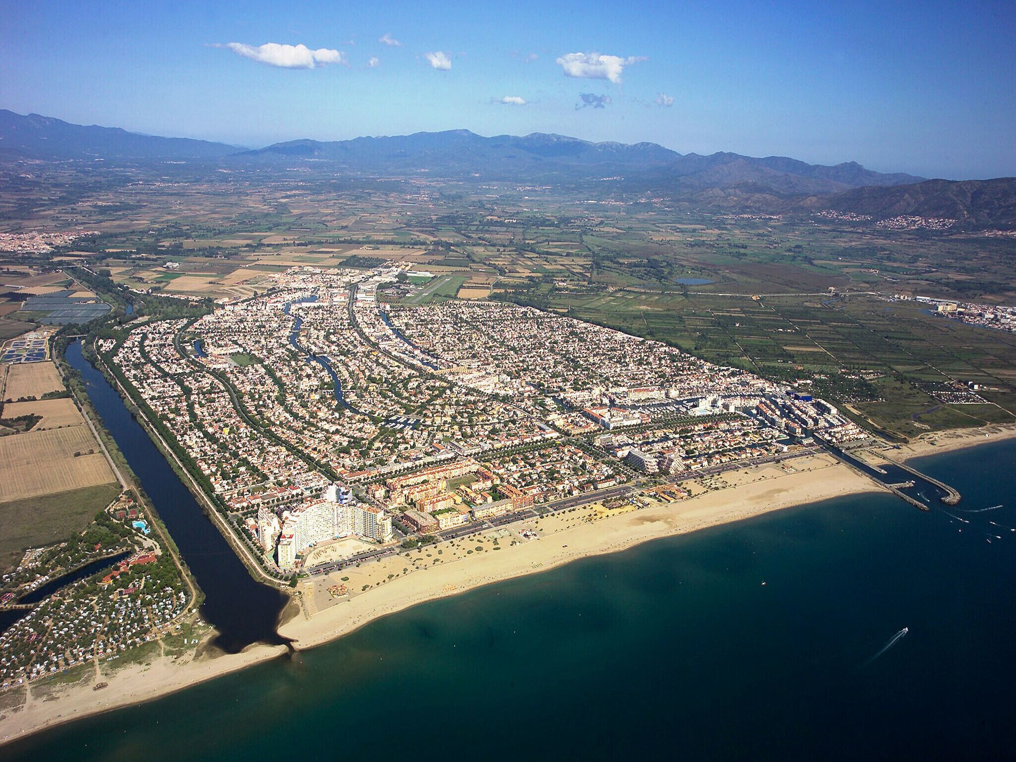 An aerial view of a coastal city with a dense urban area, a river running through it, and a beach area.