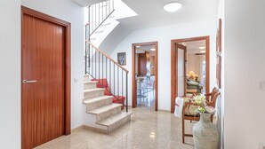 Un couloir avec une porte en bois, un escalier aux marches rouges et un coin repas avec une table et des chaises.