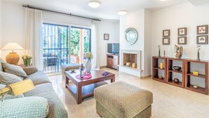 Un salon spacieux avec un canapé, une table basse et une cheminée. On peut apercevoir un téléviseur et un coin repas à travers une porte vitrée.