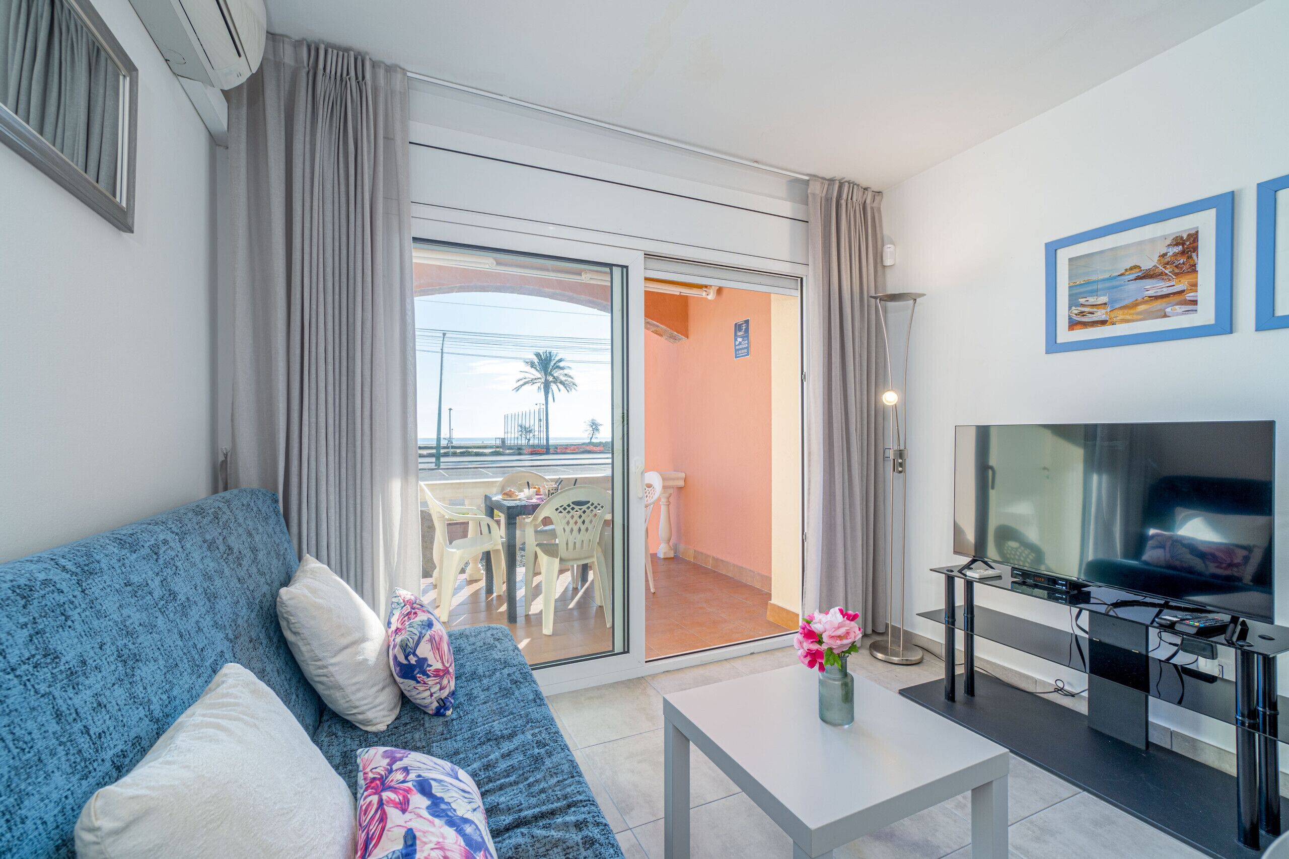 A modern living room with a blue sofa, a flat-screen TV, and a balcony with a table and chairs.