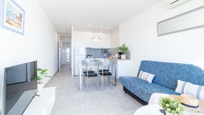 A modern living room with a blue sofa, a flat-screen TV, and a dining area with chairs and a table. - 0020-BAHIA Apartment in front of the beach with wifi (Empuriabrava)