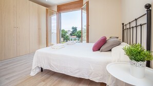 A bedroom with a large bed, a white bedside table, a potted plant, and a view of the outdoors. - 0106-LLOBREGAT House at the canal with pool and mooring (Empuriabrava)
