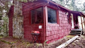Una cabaña rústica con cimientos de piedra, fachada roja y un ventanal grande.