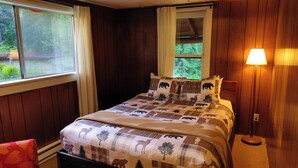 Un dormitorio con cama, ventana con cortinas, lámpara y vista a zonas verdes.
