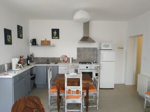 A modern kitchen with grey cabinets, a white countertop, a gas stove, a built-in oven, and a white refrigerator. There is a dining table with chairs and a coffee maker on the counter.
