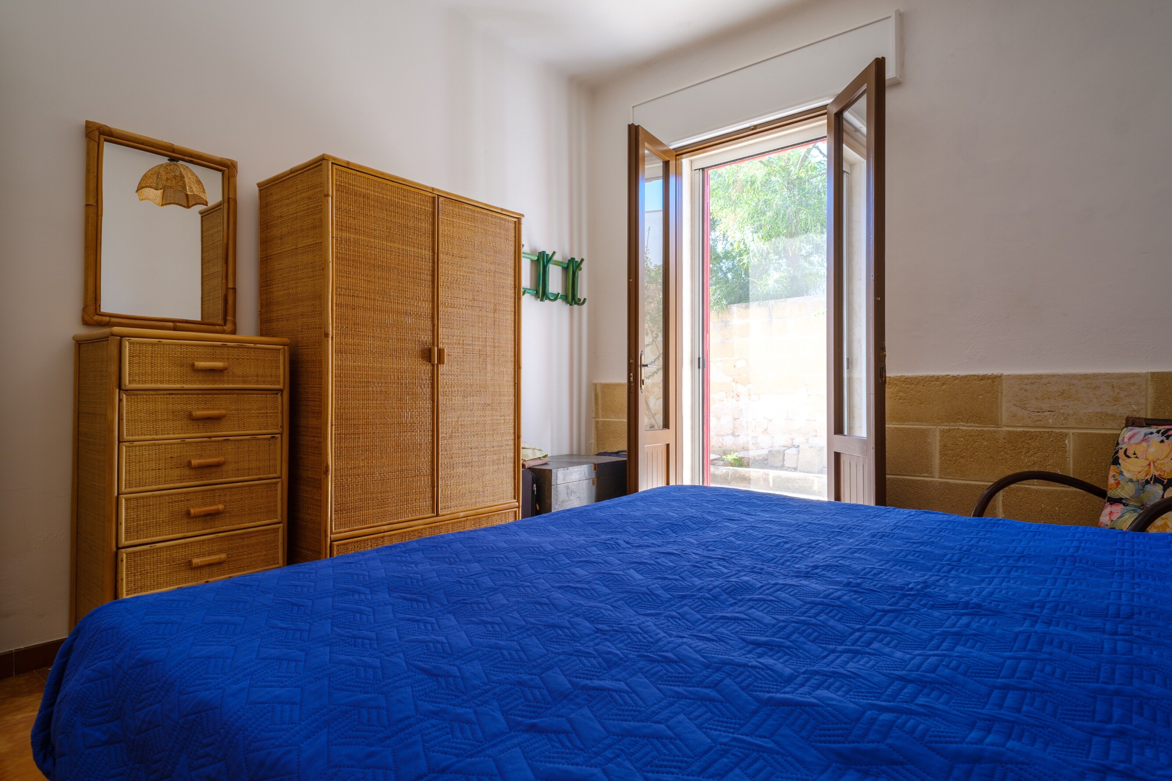 A bedroom with a bed, a wardrobe, a mirror, and a door leading to an outdoor area.