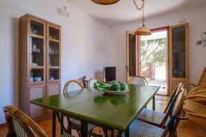 A dining area with a green table, wicker chairs, a television, and a cabinet with glass doors. - Villa "Elena" with Sea View, Terrace & A/C (Porto cesareo)