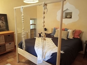 Ein Himmelbett mit weißem Makramee-Kopfstück, einer dunkelblauen Tagesdecke und vielen Kissen.