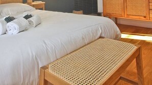 A neatly made bed with white linens and rolled towels, a wooden bench, and a wicker nightstand. - Your splendid stone farmhouse in the countryside, completely renovated (Cabris)