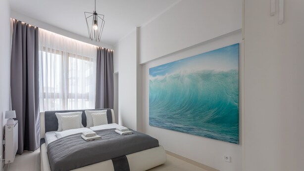 Quarto moderno com uma cama grande, uma mesa de cabeceira, uma luminária e um quadro de uma onda na parede.