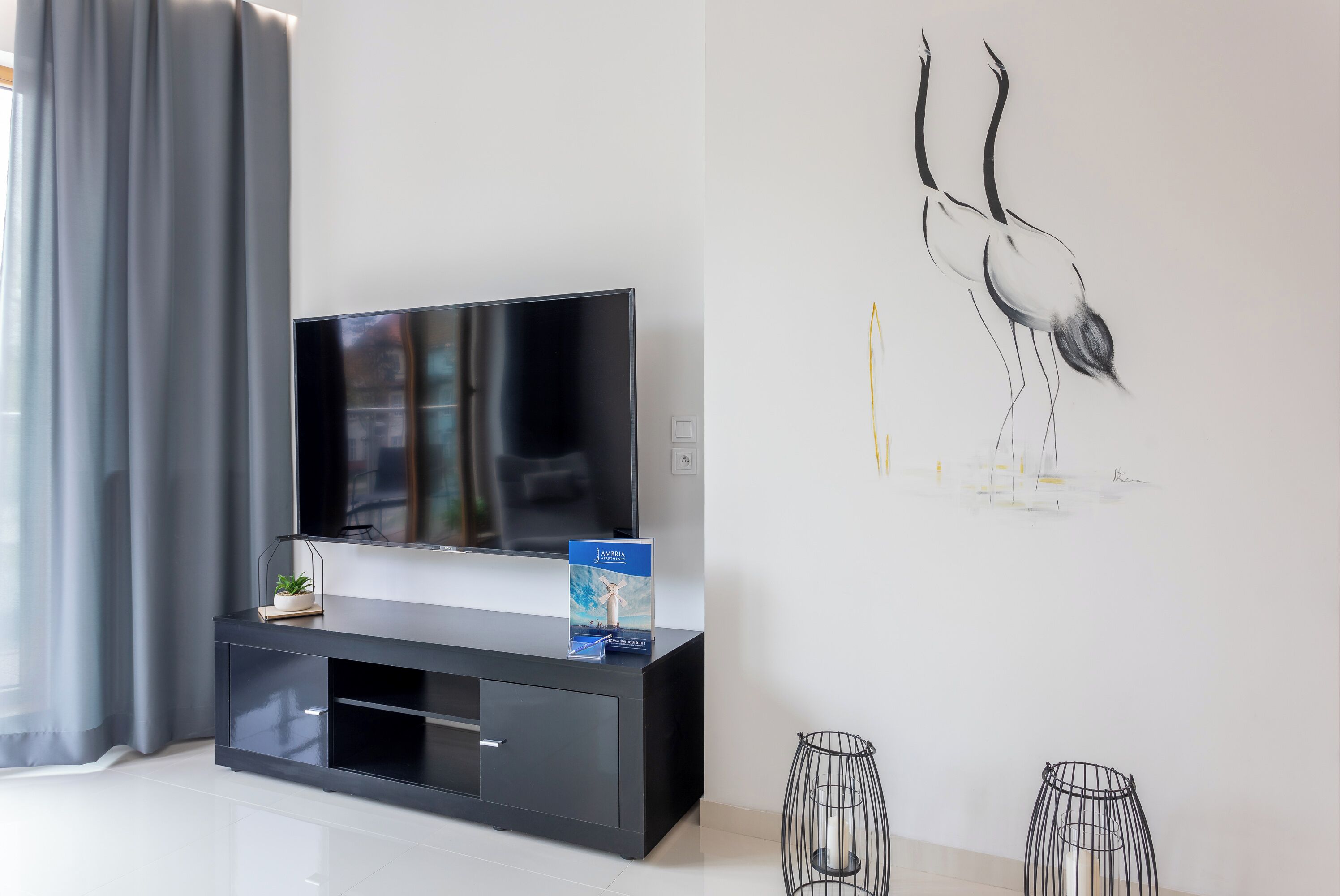 Una sala de estar moderna con un televisor de pantalla plana sobre un mueble negro, una obra de arte enmarcada en la pared y dos candelabros negros en el suelo.