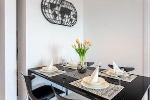 Une table à manger dressée avec de l’argenterie, des assiettes blanches et un vase de tulipes.