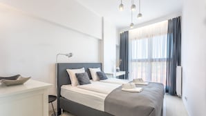 Camera d'albergo moderna con un letto grande, un comodino, una scrivania e vista sulla città attraverso tende leggere.