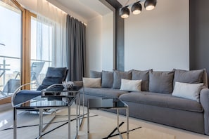 Un salon moderne avec un canapé gris, une table basse en verre et un fauteuil noir.