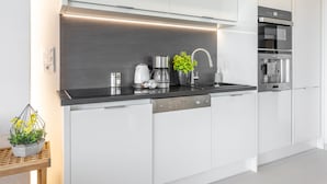 Una cucina moderna con mobili bianchi, un piano di lavoro nero, elettrodomestici in acciaio inossidabile e una piccola pianta in vaso.