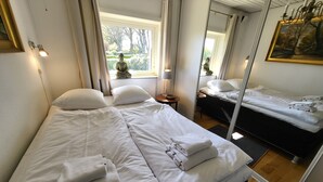 A hotel room with two beds, white linens, a large window with curtains, a painting on the wall, and a chandelier. - Kollund Cottage (Krusaa)