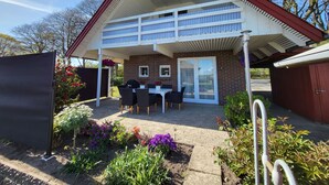 A two-story house with a covered patio, a brick exterior, and a garden with various plants and flowers. - Kollund Cottage (Krusaa)