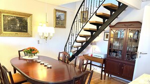 A dining area with a wooden table, chairs, and a chandelier. A staircase with a railing leads to another level. - Kollund Cottage (Krusaa)